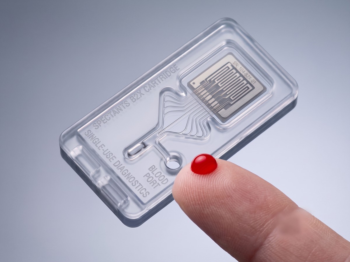 A fingertip with a drop of capillary blood at the cartridge blood port